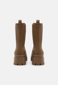 Botine din piele maro până la gleznă, cu o talpă platformă groasă și o ușoară textură, prezentând cusături verticale și taburi de prindere în spate.