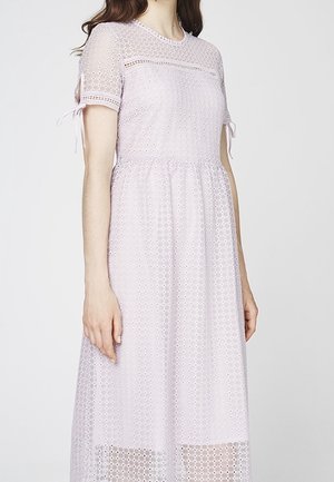 Vrouw draagt een lichtpaarse, korte mouwen, knie-lange jurk van eyelet-stof met kleine strikdetails aan de mouwen.