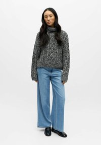 Chunky strikket genser med rullekrage i grått og svart, kombinert med vide lyseblå denimjeans og svarte loafers. Detaljer med teksturert mønster.