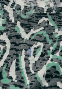 Tejido texturizado con un patrón abstracto en gris, blanco y verde. El diseño presenta líneas onduladas y formas en diferentes tonos y contrastes.