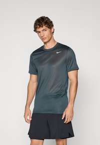 Lühikeste varrukatega tumeteal värvi kerge spordit-särk, mis on valmistatud siledast kangast. Rinnal on väike valge Nike'i logo.