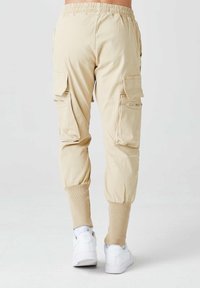 Beige cargo-housut, joissa on joustava vyötärö, ribbatuletut nilkat ja sivutaskut, valmistettu kevyestä kankaasta.