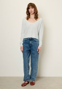 Un pull cropped bleu clair en matériau doux, associé à un jean en denim bleu taille haute et des sandales tissées marron. Design et texture simples.