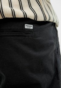 Crne pamučne hlače s glatkom teksturom, s leđa imaju džep i uz etiketu Jack & Jones ušivenu na njima. Uparene su sa prugastim pletenim topom.