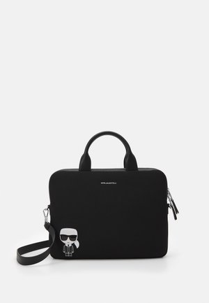 Bolso rectangular negro con asas superiores, correa de hombro desmontable, pequeña figura de dibujos animados con gafas de sol, y logo de Karl Lagerfeld.