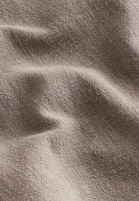 Tela de color marrón claro con textura y un sutil patrón tejido, que muestra pliegues suaves y ondulados y una apariencia natural ligeramente jaspeada.