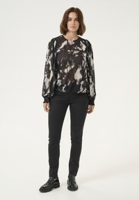 Sheer black and white tie-dye blouse with long, puffed sleeves, gathered cuffs, round neckline, and flowing fit paired with black skinny jeans and shoes.