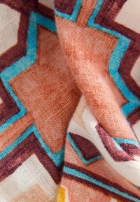 Textil med ett geometriskt mönster i nyanser av brunt, turkos och kräm. Tyget har en mjuk textur med synlig väv.