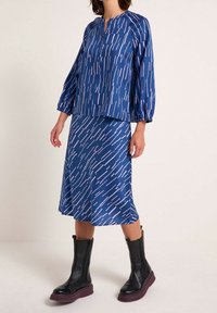 Blå mønstret bluse med trekvartærmer parret med en matchende blå nederdel. Båret med knæhøje sorte støvler og en kraftig lilla sål.