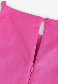 Rosa linne tyg med en synlig bakdragkedja och en liten matchande knapp vid kragen. Slät textur, skräddarsydd design och rena linjer.