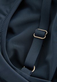 Inredning av en marinblå ryggsäck med texturerat nätmaterial, justerbar rem med en metallisk D-ring spänne och mjukt foder.