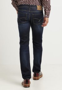 Mörkblå denimjeans med slim fit, med två bakfickor och kontrasterande sömnad, matchade med bruna skor.