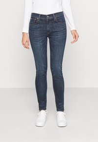 Mörkblå skinny jeans i denim med medelhög midja, fem fickor och subtila sömnadsdetaljer. Matchas med vita sneakers.