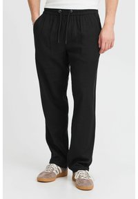 Black linen trousers with an elastic waistband, drawstring detail, and a relaxed fit. Paired with brown and white sneakers.