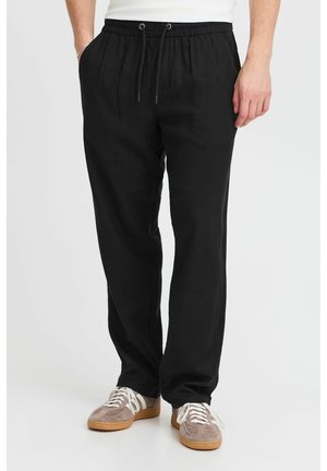 Pantalones de lino negros con una cinturilla elástica, detalle de cordón y un corte relajado. Combinados con zapatillas marrones y blancas.