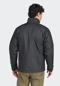 Black puffer jacket with a high collar, featuring quilted texture and a slim fit design; paired with khaki pants, viewed from the back.