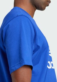 Blue cotton t-shirt with a crew neckline. Features short sleeves and a prominent white logo on the front. Smooth texture and fitted design.