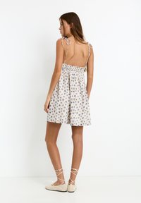Vestito stampato floreale in beige chiaro, con spalline sottili e schiena arricciata, e una gonna fluente che arriva a metà coscia.