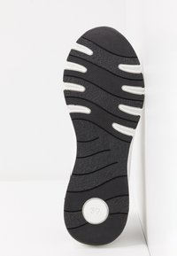 Sole černo-bílé tenisky s texturovaným gripem a velikostním indikátorem "37" v kruhové bílé oblasti blízko paty, na bílém pozadí.