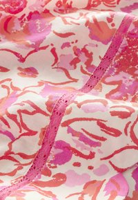 Kvietkovaná látka v odtieňoch ružovej a červenej s krémovým pozadím, zdobená jemnou čipkou pozdĺž švu.