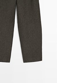 Partie inférieure d'un pantalon droit marron foncé texturé sur fond blanc.