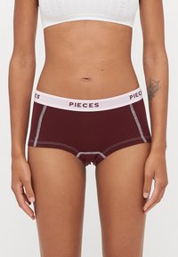 Burgundské panty s bílým prošitím a růžovým pasem s logem "PIECES". Bavlněný materiál, pohodlný design, střední výška.
