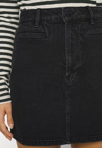 Jupe en denim noir avec une taille ajustée, des poches avant et une texture subtile. L'ourlet est droit et se termine au-dessus du genou.