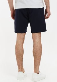 Bermudas de algodón en color navy con un ajuste relajado, que cuentan con una cintura elástica y bolsillos laterales, combinadas con zapatillas blancas.