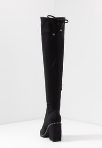 Schwarze kniehohe Stiefel mit schickem Stofffinish, ausgestattet mit einem gebundenen Riemen oben und Nietenverzierungen auf dem Blockabsatz.