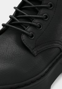Bottine en cuir noir avec une surface texturée, six œillets avec des lacets plats noirs et une semelle en caoutchouc robuste.