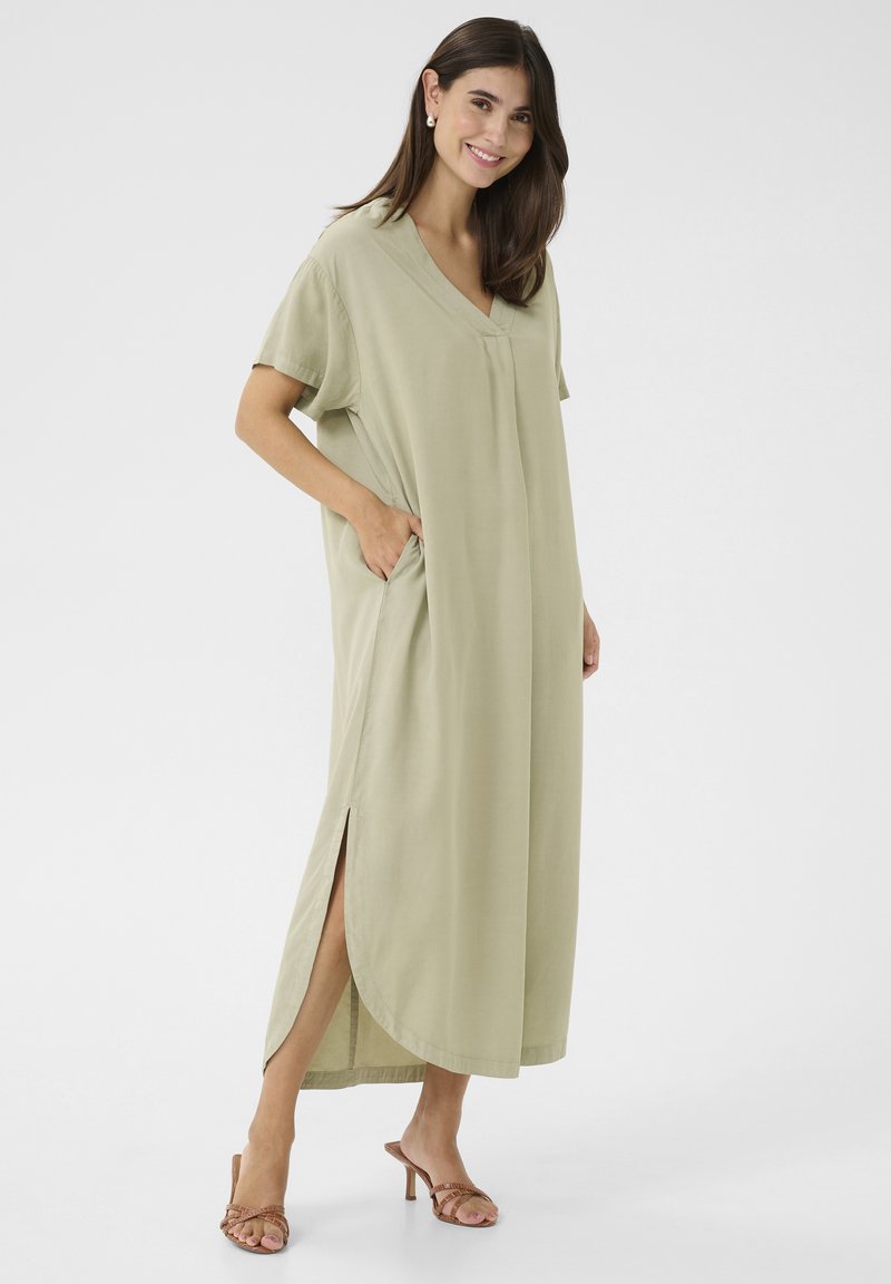 Térd hosszúságú, világos zöld ruha puha anyagból, V-nyakkivágással, rövid ujjal, oldalsó zsebekkel és oldalsó hasítékokkal a könnyű mozgás érdekében.