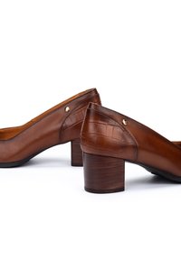 Chaussures en cuir marron avec un talon embossé crocodile, à petit talon carré et accent métallique, présentant une texture lisse et un design classique.