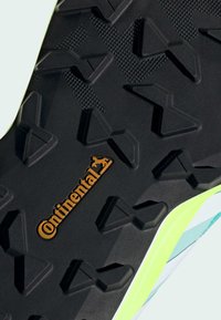Juodas gumos batų padas su daugiareikšmiais protektoriais, kuriame yra oranžinė "Continental" logotipo detalė ir ryškiai žalia akcento juosta palei kraštą.