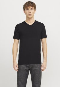 T-shirt noir à col en V, confectionné en tissu doux avec des manches courtes, présentant une coupe ajustée et une texture lisse. Porté avec un jean foncé.