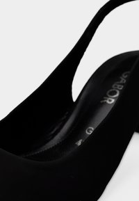 Μαύρο παπούτσι slingback με λείο συνθετικό υλικό, στρογγυλεμένη μύτη και διακριτική σήμανση στην πάτημα. Ο πλαϊνός σχεδιασμός με ανοίγματα προσφέρει κομψή εμφάνιση.