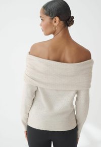 Maglione leggero beige off-shoulder con orlo a costine, texture a pois e morbido materiale di maglia, visto da dietro.