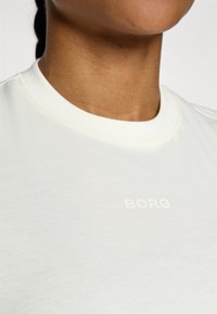 Bijela pamučna majica s okruglim izrezom, koja ima suptilnu teksturiranu završnicu i mali, svijetlosivi logotip "BORG" na prsima.