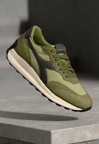 Olive green sneakers with a mix of suede and mesh upper. Features grey accents, perforated design, and a cushioned, off-white sole.