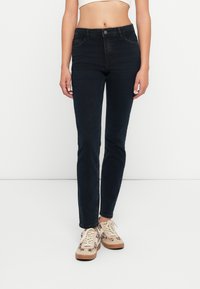Sötétkék farmer skinny farmernadrág, magas derekú, elülső zsebekkel, krém színű sportcipőkkel párosítva, virágmintával és bézs részletekkel.