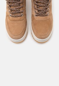 Brune ruskind høje sneakers med teksturerede snørebånd og metaløjer, der har en hvid gummisål og en gummibund for godt greb.
