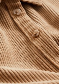 Gros plan d’un tissu en velours côtelé marron clair avec des rainures verticales et deux boutons ronds marron cousus.