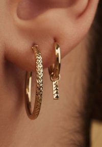 Goldene Creolen mit strukturiertem Muster, dazu ein kleinerer verbundener Ohrring mit einem diamantenförmigen Akzent.