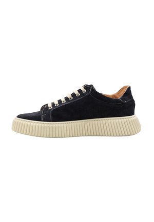 Sneaker in suede nero a taglio basso con suola beige spessa e rigata e lacci bianchi, vista laterale su sfondo bianco.