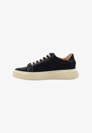 Sneaker in suede nero a taglio basso con suola beige spessa e rigata e lacci bianchi, vista laterale su sfondo bianco.