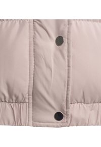 Närbild av blekrosa quiltat tyg med vertikal söm och två glänsande svarta tryckknappar.