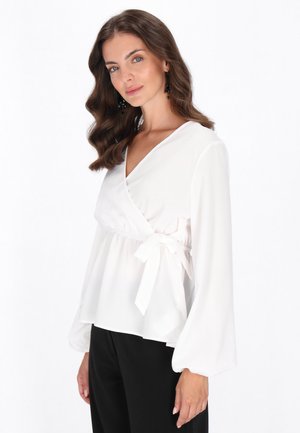 Witte wikkelblouse van lichtgewicht stof, met lange mouwen, een gestrikt taille-detail en een V-hals ontwerp. Zwarte broek completeert de outfit.