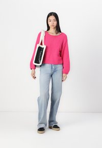 Bright pink knitted sweater with balloon sleeves, paired with light blue flared jeans and black sneakers. Bag features a black panel with fluffy edges.