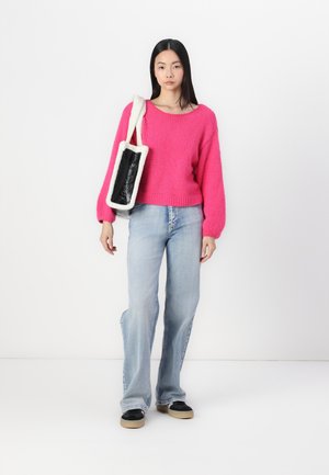 Pull en tricot rose vif avec des manches ballon, associé à un jean flair bleu clair et des baskets noires. Le sac présente un panneau noir avec des bords duveteux.