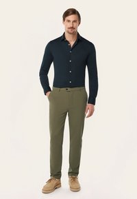 Marineblauw overhemd met lange mouwen en knopen, olijfgroene snitbroeken en beige schoenen. Gladde stoftextuur met een aansluitende pasvorm en gestructureerde silhouet.