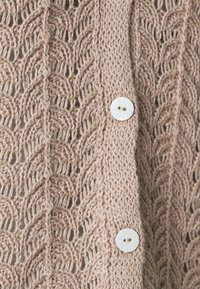 Beige strikket cardigan med blondermønster, med en glatt tekstur og en enkel hvit knappelukking foran.